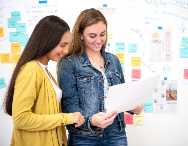 Two women in front of a white board brainstorming ideas. 